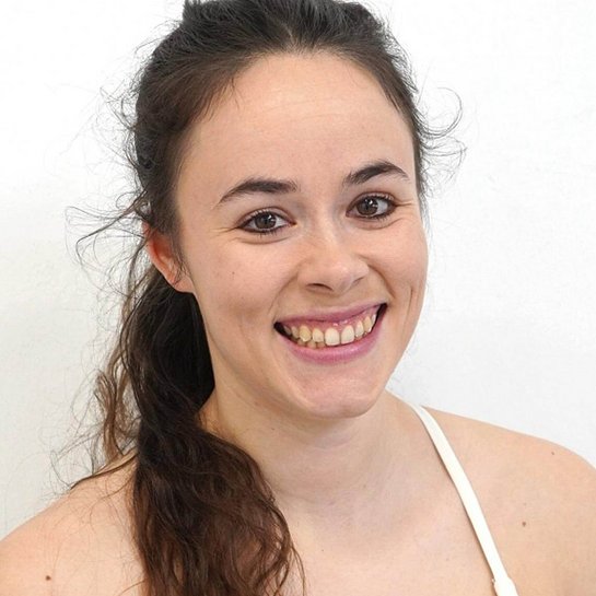 Portrait der Rhönrad-Sportlerin Larissa von Behren, lächelnd in die Kamera blickend, mit einem weißen Oberteil vor neutralem Hintergrund.