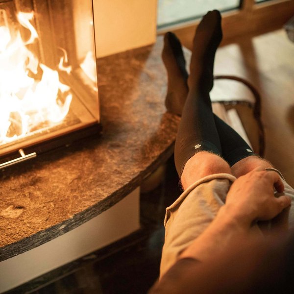 Ein Mann sitzt mit kalten Füßen und Kompressionsstrümpfen vor dem Kamin.