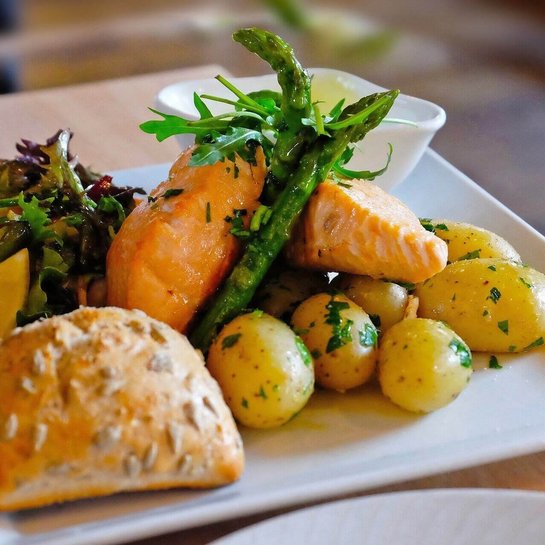Empfohlene Ernährung bei Arthrose Das Bild zeigt einen Teller mit Lachs, Kartoffeln, einem Brötchen und Gemüsebeilage. Die Ernährungsweise spielt bei einer Arthrose eine wichtige Rolle.