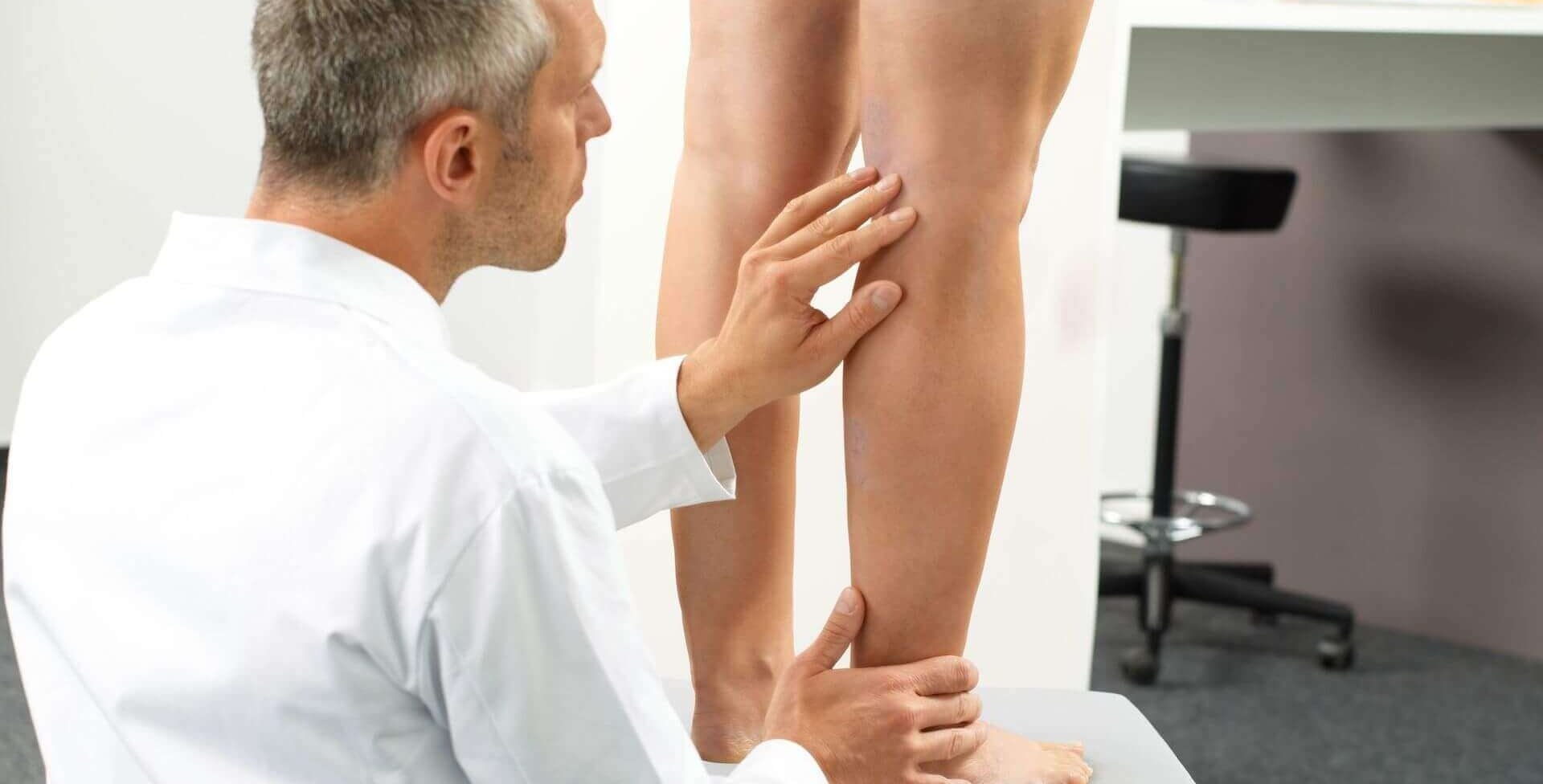 Das Bild zeigt einen Arzt, der die Beine einer Patientin untersucht, welche auf einem Hocker vor ihm steht. Die Diagnose eines Lip- oder Lymphödems sollte bei einem Facharzt erfolgen.