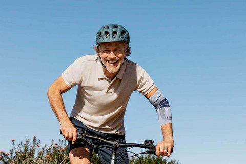 Das Bild zeigt einen Mann, der mit einem Fahrrad in den Bergen unterwegs ist und dabei eine EpiTrain Bandage trägt, um Ellenbogenschmerzen zu lindern.