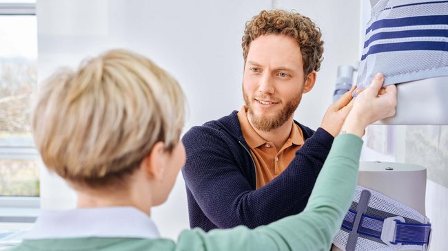 Ein Berater zeigt einer interessierten Patientin die Rückenbandagen von Bauerfeind in einem Showroom.