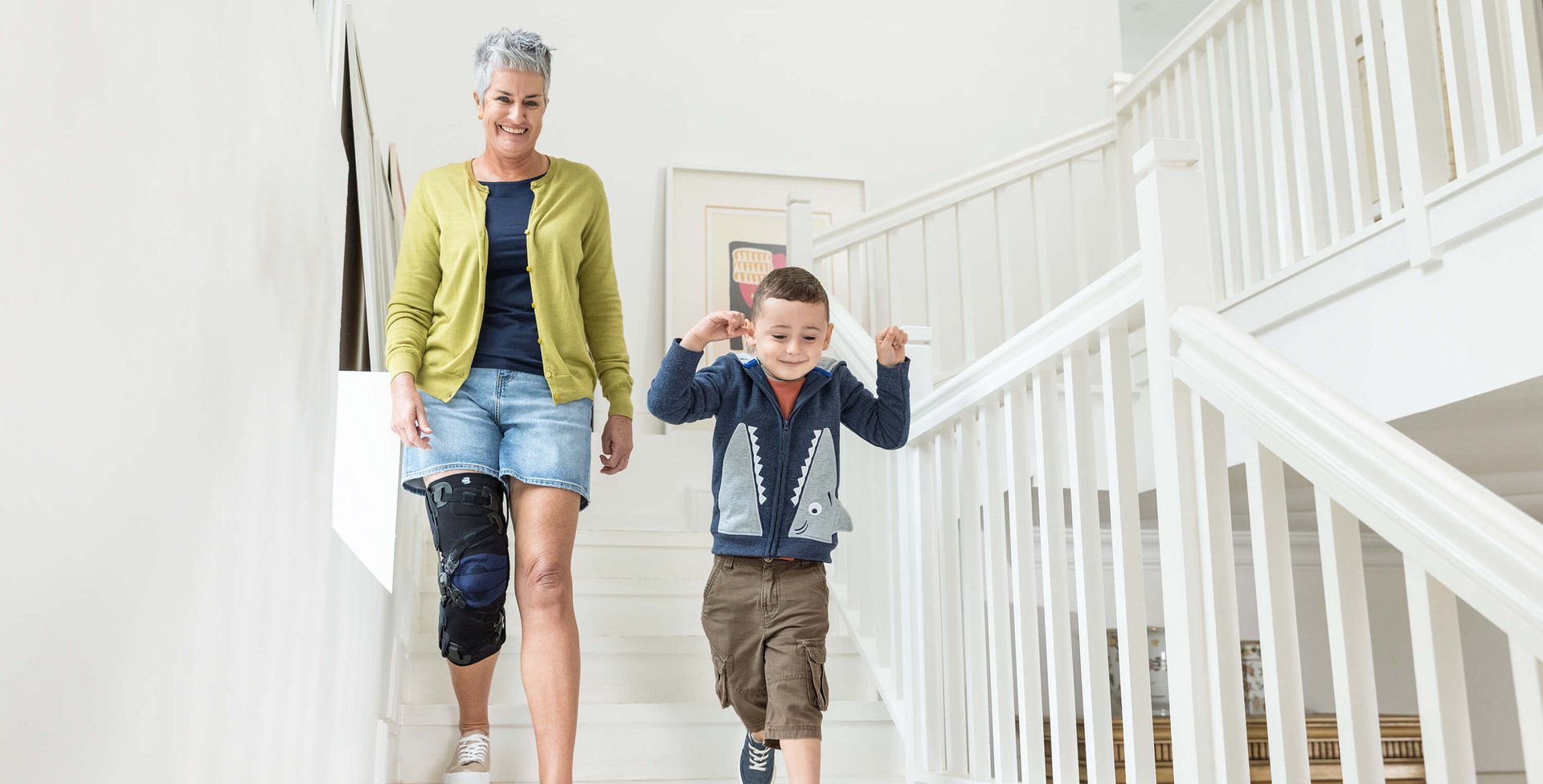 Das Bild zeigt eine Dame mit ihrem Enkel beim Herunterlaufen einer Treppe. Zur Unterstützung ihres Knies trägt die Frau eine Gonarthrose-Orthese von Bauerfeind, die GenuTrain OA.