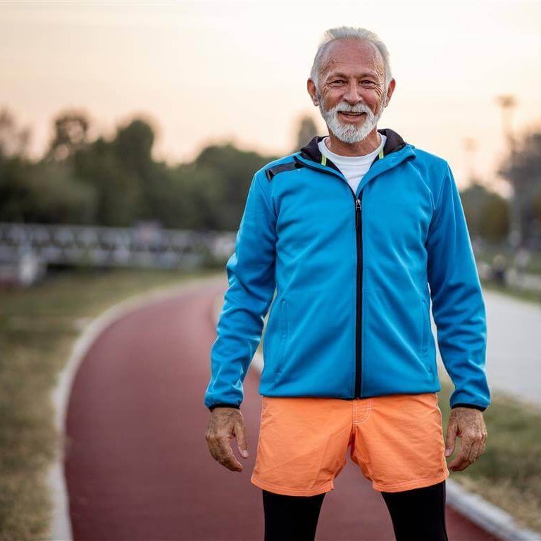 Das Bild zeigt einen älteren Mann in einem Sportoutfit auf einem Sportplatz. Er bleibt in Bewegung, um gegen arthrosebedingte Schmerzen im Griff zu behalten.