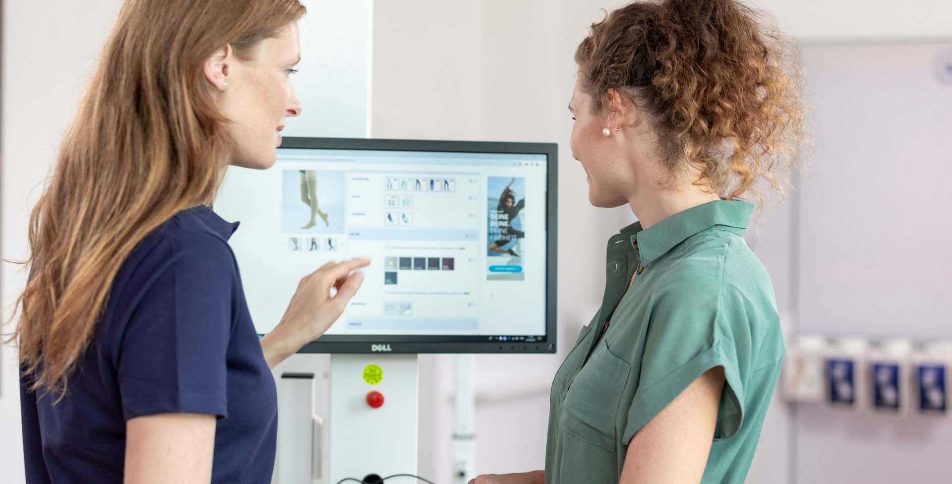 Zwei Mitarbeiterinnen des Bauerfeind Kundenservice stehen vor einem Computerbildschirm, auf dem eine Produktübersicht zu sehen ist, und besprechen individuelle Anpassungsmöglichkeiten für Kompressionsprodukte.