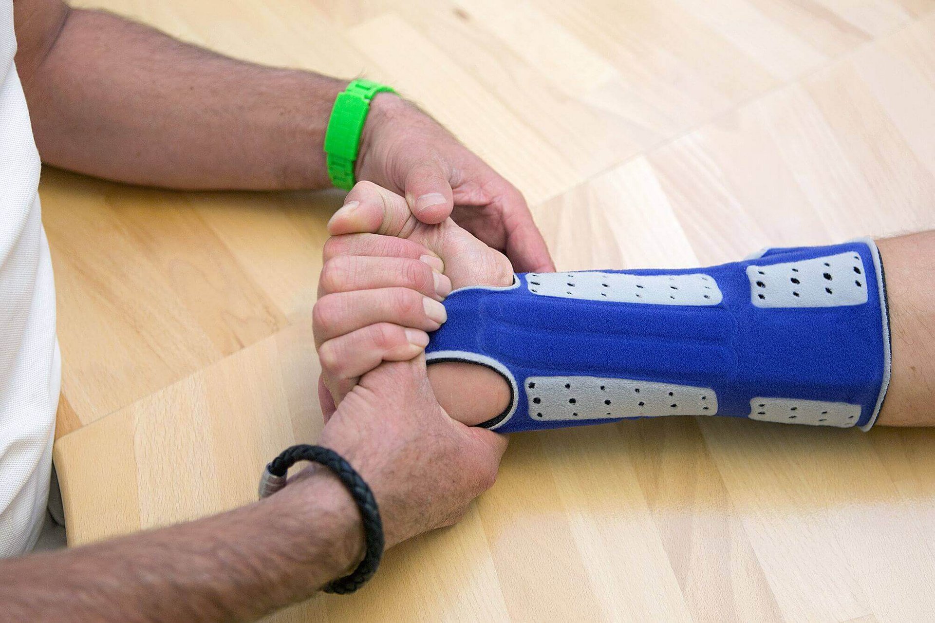 Auf dem Bild führt ein Therapeut mit einem Patienten Übungen für das Handgelenk durch. Der Patient trägt eine ManuLoc long, eine stabilisierende Handorthese von Bauerfeind.