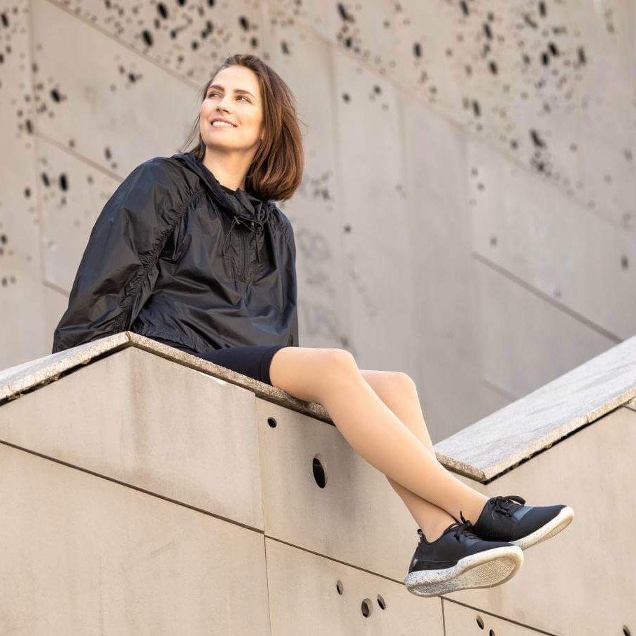 Eine Frau sitzt auf einer Steinmauer von einer Treppe. Sie trägt VenoTrain micro Kompressionsstrümpfe von Bauerfeind.