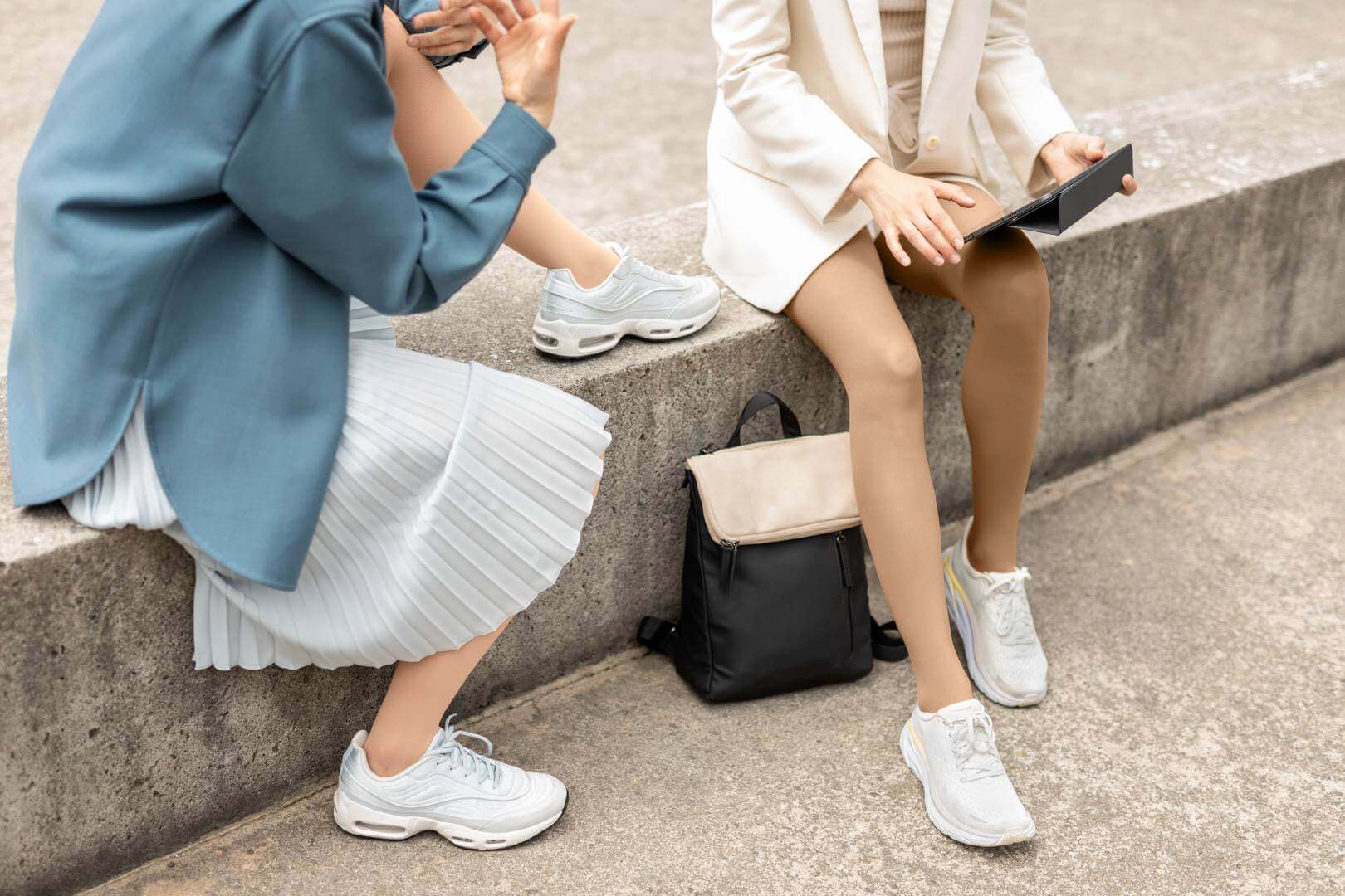Zwei Frauen sitzen auf einer Steinmauer. Der Fokus liegt auf ihren Beinen, denn sie tragen VenoTrain micro Kompressionsstrümpfe von Bauerfeind.b