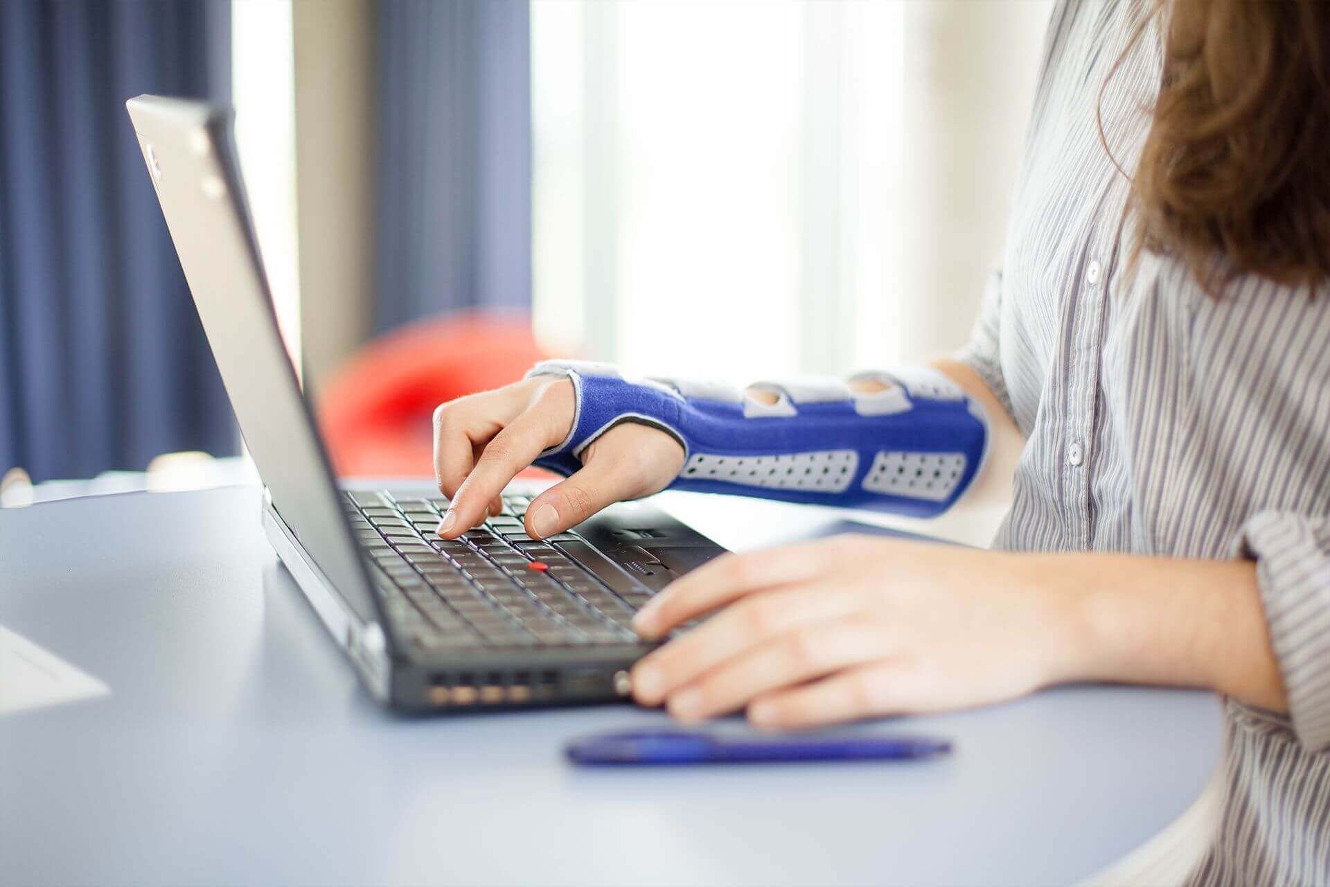 Bildausschnitt einer Frau beim Arbeiten am Laptop. Sie trägt eine ManuLoc long, eine stabilisierende Handgelenksorthese von Bauerfeind, am rechten Arm. Diese bietet u.a. nach einer Radiusfraktur Unterstützung.